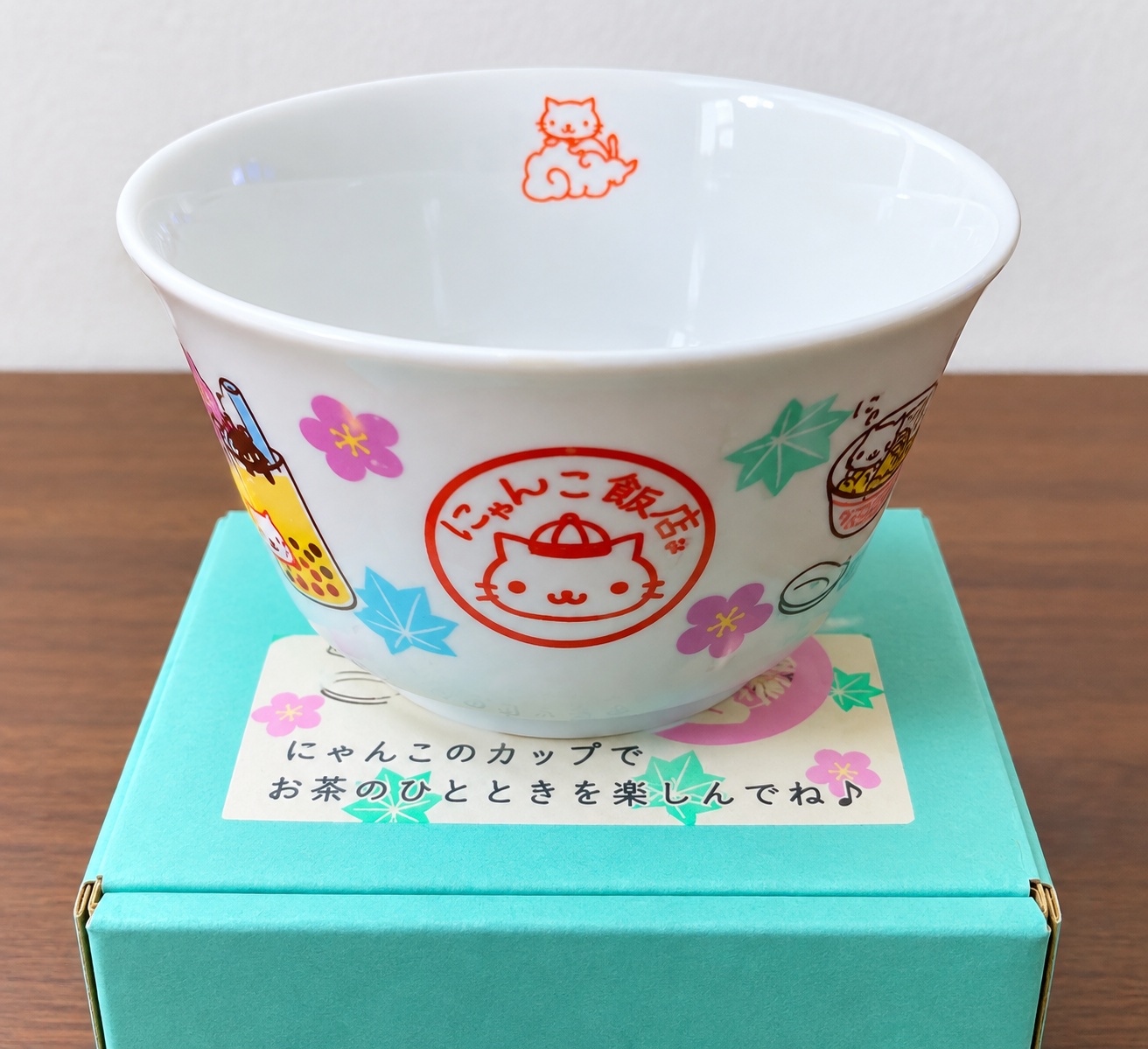 Nyanko Hanten Japanese Small Yunomi Tea CupA cute Japanese Nyanko Hanten (にゃんこ飯店) ceramic yunomi featuring adorable cat characters with colorful seasonal floral designs.